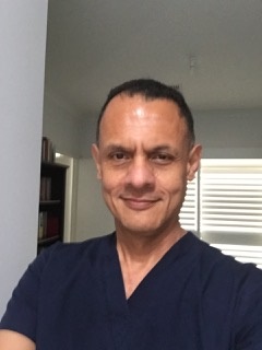 Dr Stephen Southgate smiles at the camera whilst wearing dark navy scrubs